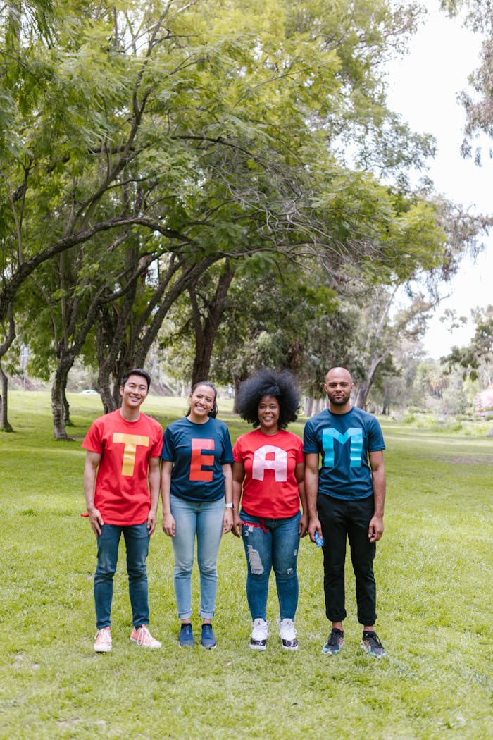 about-us A diverse group of adults wearing TEAM shirts standing in a park.